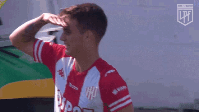 a man wearing a red and white shirt with the letter h on it covering his eyes