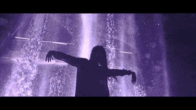 a woman is standing in front of a fountain with her arms outstretched in the dark .