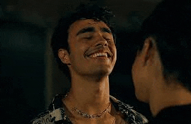 a man and a woman are looking at each other and smiling . the man is wearing a necklace .