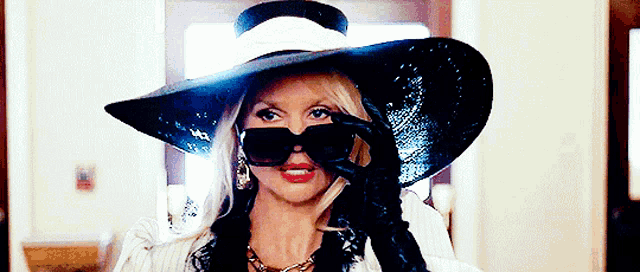 a woman wearing a hat and sunglasses is holding a cigarette in her mouth .