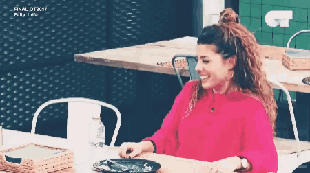 a woman in a pink sweater is sitting at a table with a plate of food on it