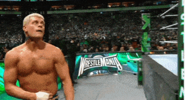 a shirtless wrestler is standing in front of a wrestlemania sign .