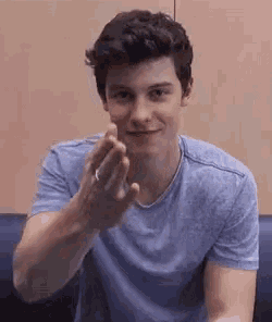 a young man wearing a blue shirt is sitting on a couch and making a heart shape with his hands .