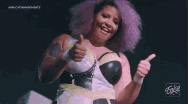 a woman with pink hair gives a thumbs up in front of a sign that says enjoy