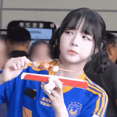 a girl in a blue and yellow jersey is eating a skewer