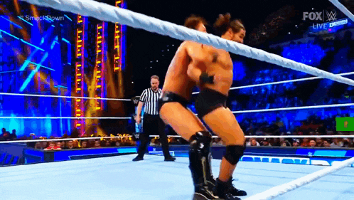 two men are wrestling in a ring with a referee in the background .
