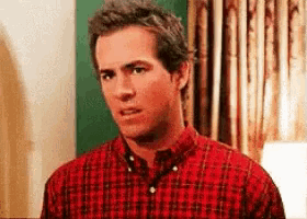 a man in a red plaid shirt is making a funny face in a room .