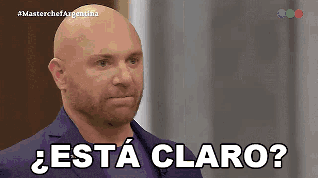 a bald man with a beard says " esta claro " while wearing a blue suit