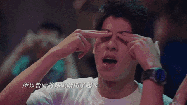 a man in a white shirt is rubbing his eyes with his fingers
