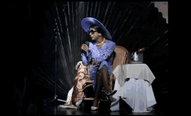 a woman is singing into a microphone while wearing sunglasses and a necklace .