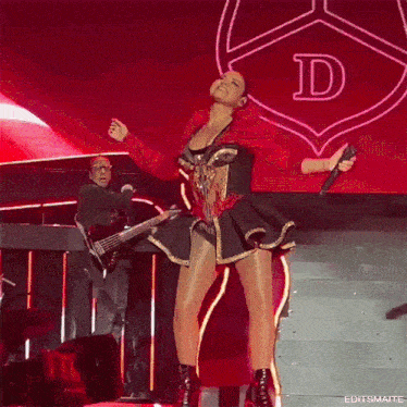 a woman holding a microphone on a stage with a letter d in the background
