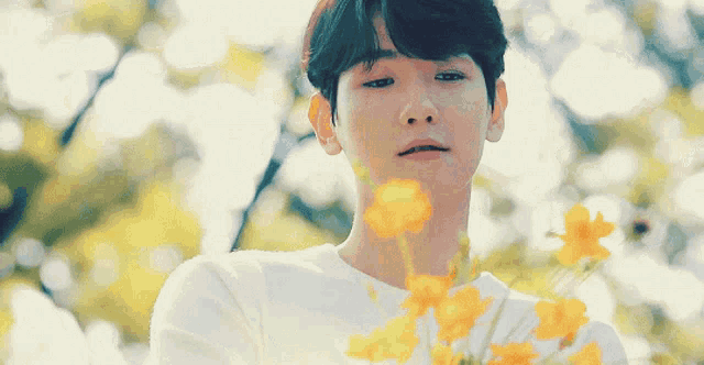a young man wearing a white shirt with yellow flowers on it looks at the camera