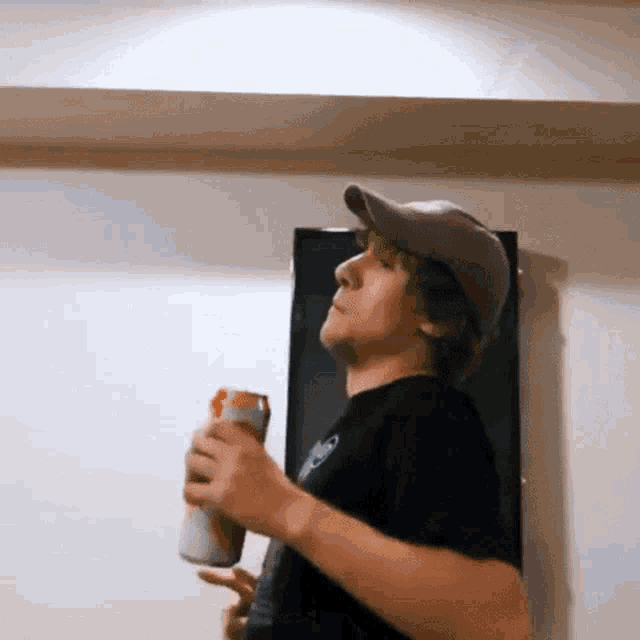 a man with green hair is holding a can of soda in front of a television .