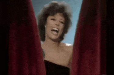 a woman in a black dress is laughing and standing behind a red curtain .