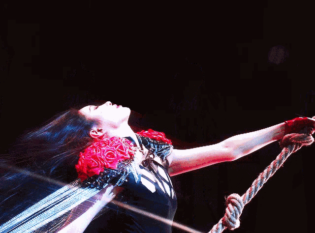 a woman in a black dress with red roses on her shoulders is holding a rope