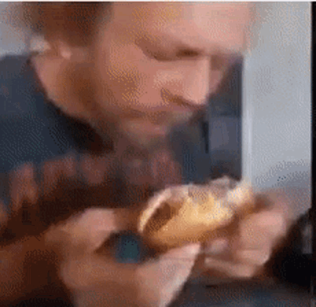 a man with a beard is eating a hamburger with a bite taken out of it .