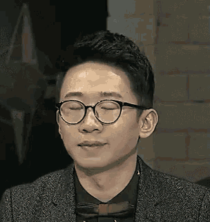 a man wearing glasses and a suit is making a funny face with his eyes closed .