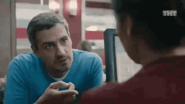 a man in a blue sweater is talking to a woman in a red shirt .