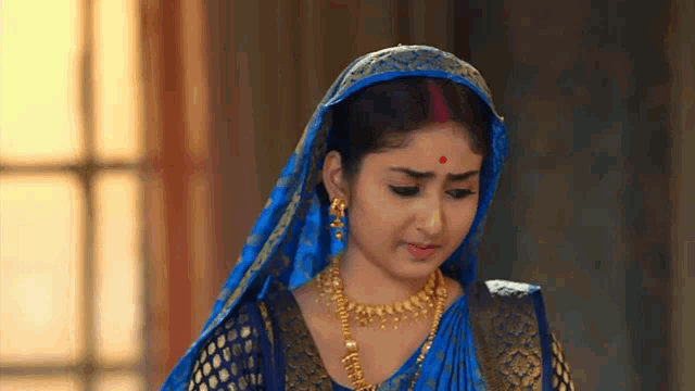 a woman wearing a blue and gold saree and gold jewelry .