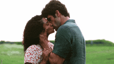 a man and a woman are kissing in a grassy field