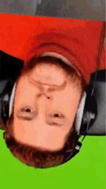 a man is wearing headphones and laying upside down on a green screen .