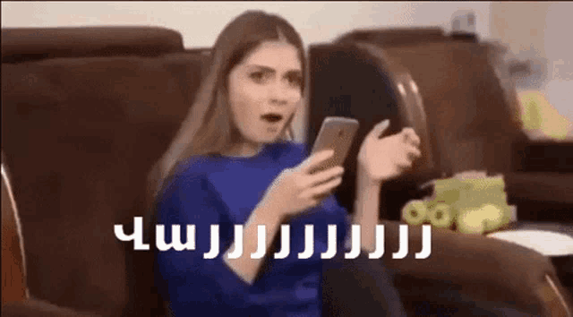a woman is sitting on a couch holding a cell phone and making a funny face .