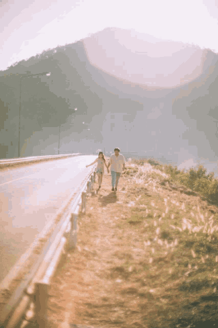 a man and a woman are holding hands while walking down a road