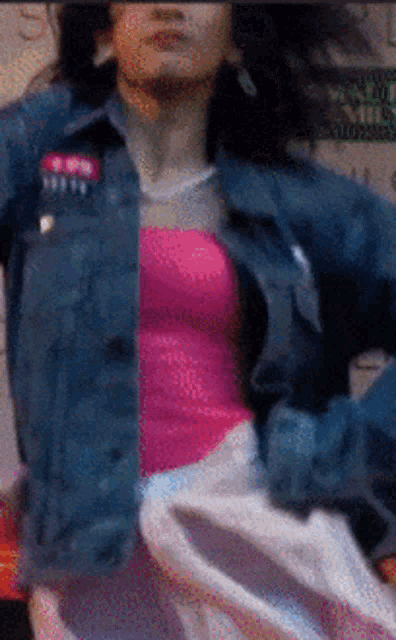a woman wearing a denim jacket and a pink tank top is dancing