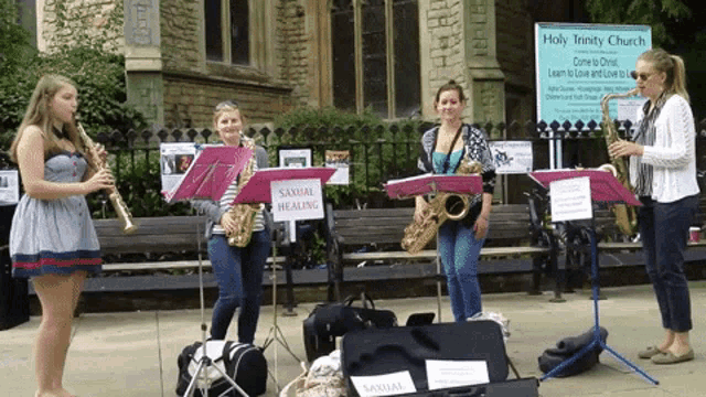a group of women playing saxophones in front of a holy trinity church sign