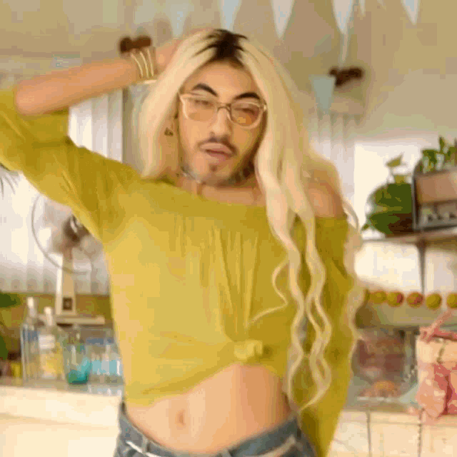 a man with blonde hair and glasses is wearing a crop top and shorts