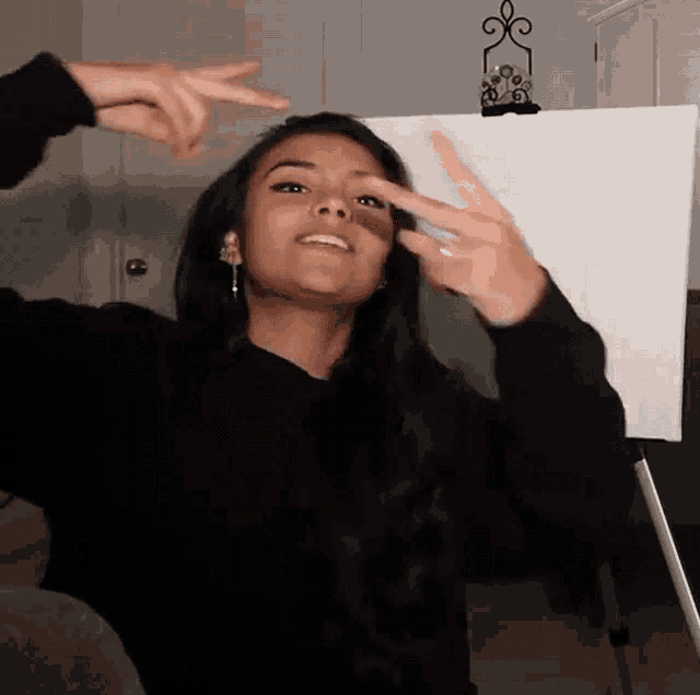 a woman in a black sweater is making a peace sign with her fingers