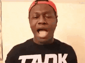 a man wearing a hat and a tank shirt is sticking his tongue out .
