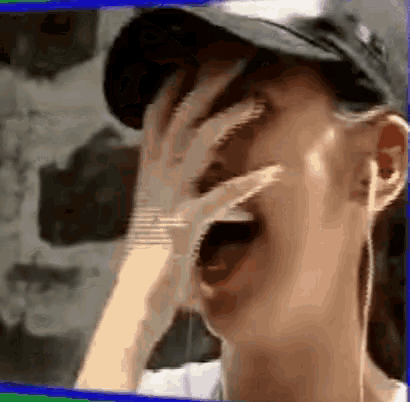 a man wearing a hat is covering his face with his hand .