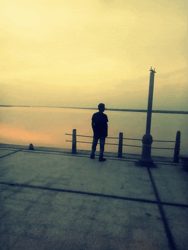a man in a hat stands on a dock looking out over a body of water