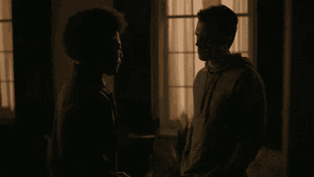 two men standing next to each other in front of a window in a dark room