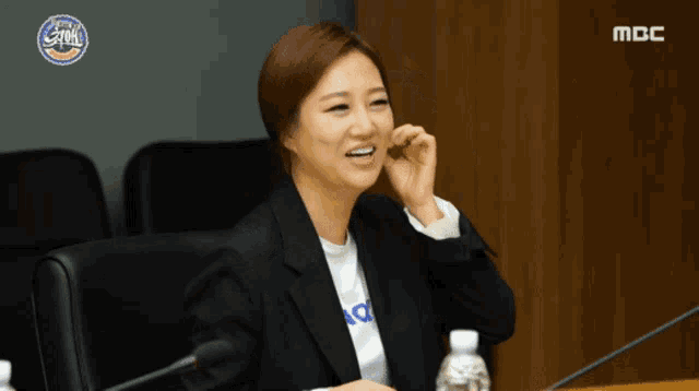 a woman sitting at a desk with a mbc logo in the background