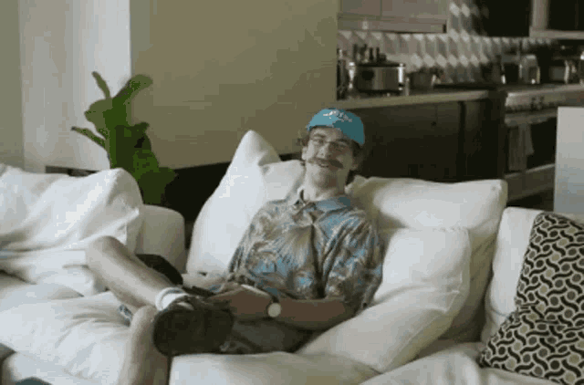 a man is sitting on a couch wearing a blue hat that says scott