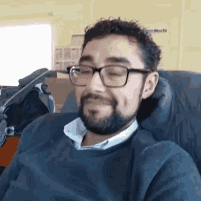 a man with a beard and glasses is sitting in a chair with his eyes closed and smiling .