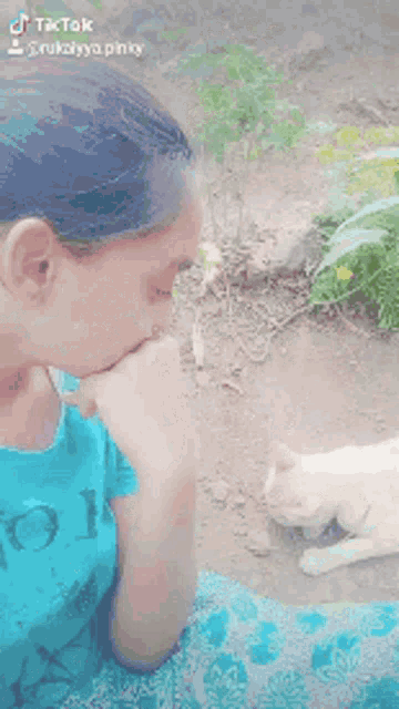 a girl in a blue shirt is playing with a cat outside