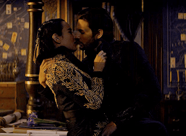 a man and a woman are kissing in a dark room with papers on the table
