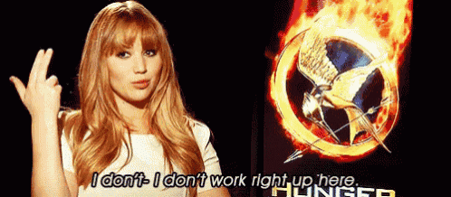 a woman is making a middle finger gesture in front of a poster for the hunger games .