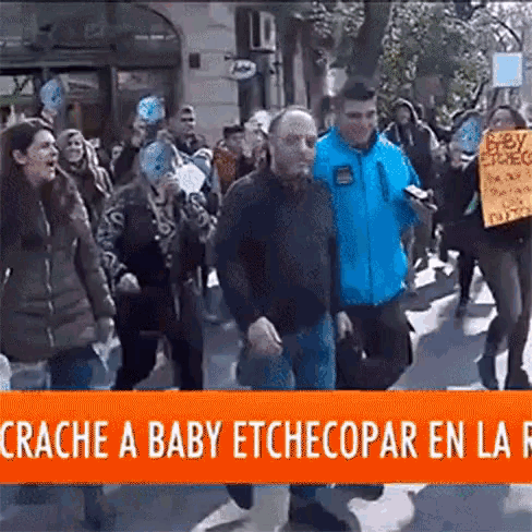 a group of people walking down a street with a sign that says crache a baby etchecopar en la r