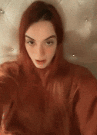 a woman with red hair is taking a selfie while wearing a hoodie .
