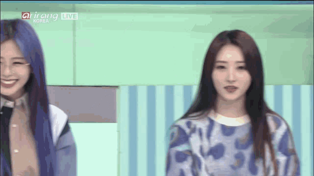 a girl with purple hair is smiling in front of a screen that says arirang live