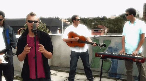 a man singing into a microphone while a man playing a guitar and another man playing a keyboard