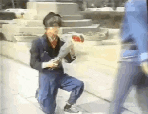 a man is kneeling down on the sidewalk holding a bouquet of flowers and a sword .