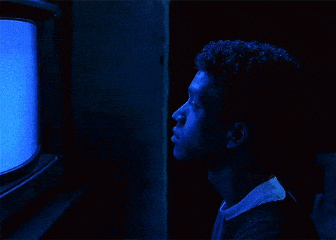 a man is sitting in front of a television in a dark room .