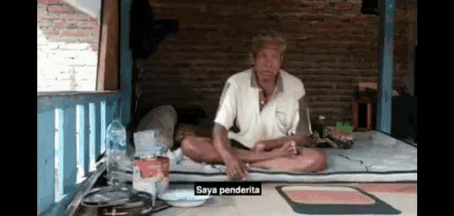 a man sits on a bed with the words saya penderita written below him