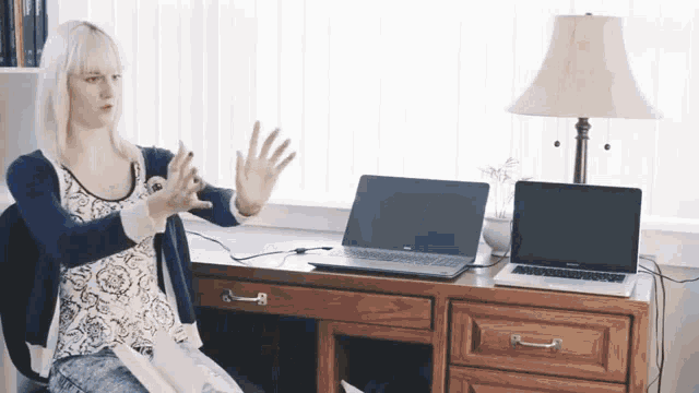 a woman sitting at a desk with two laptops on it