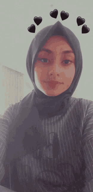 a woman wearing a hijab takes a selfie with hearts on her head
